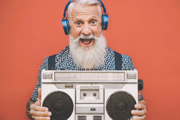 Happy senior man listening to music with boombox and headphones outdoor - Crazy hipster male having fun with vintage stereo - Concept of elderly people lifestyle
