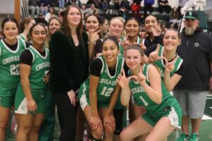 girls basketball team in green and white uniforms posing for a picture with coach in all black suit